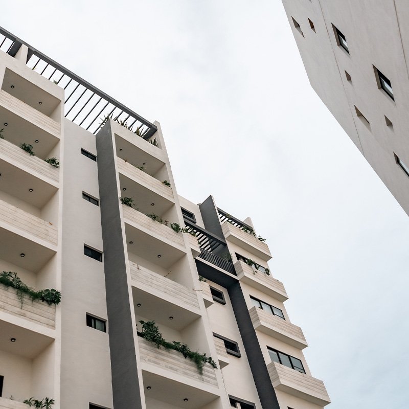 Edificio de departamentos en Cancún visto desde abajo, con balcones, jardineras y acabados en piedra clara