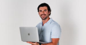 Victor Ruiz, broker inmobiliario en Cancún, de pie sosteniendo una laptop sobre fondo blanco